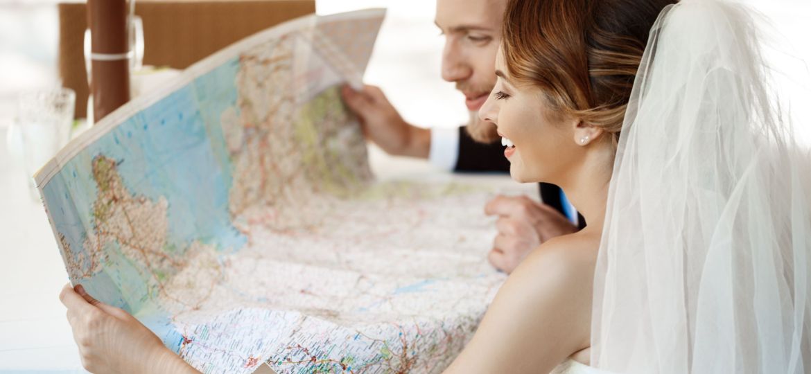 Young beautiful newlyweds smiling, choosing honeymoon trip, looking at map.